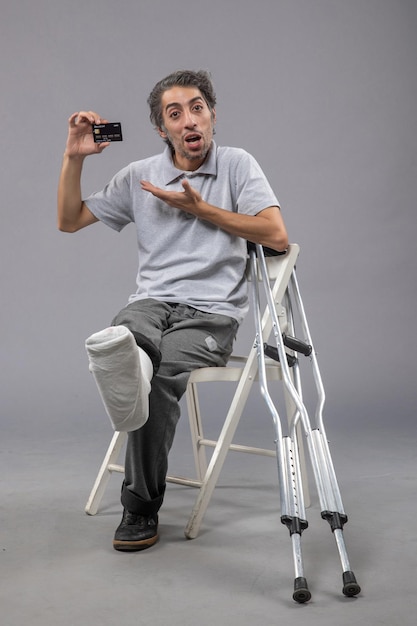 Foto grátis jovem do sexo masculino com o pé quebrado e bandagem segurando o cartão do banco preto na mesa cinza torção do sexo masculino com dor no pé acidente