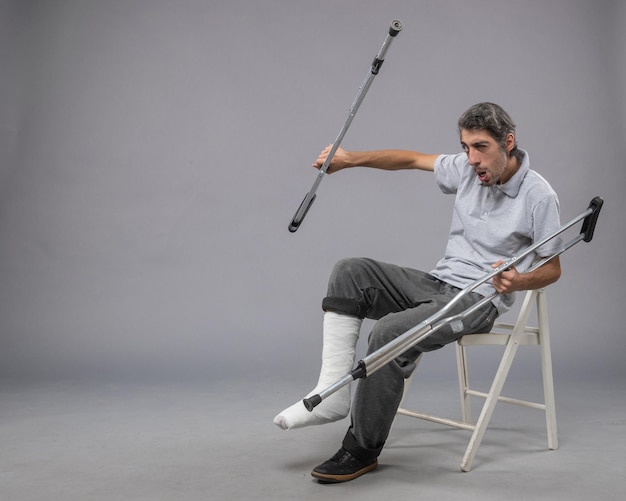 Foto grátis jovem do sexo masculino com o pé quebrado usando muletas para andar sobre um piso cinza.
