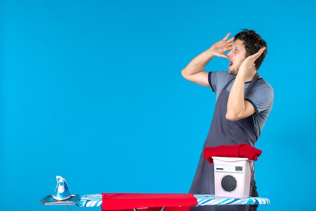 Jovem do sexo masculino com tábua de passar roupa em um fundo azul cor de ferro de lavar roupa máquina de lavar trabalho doméstico homem de frente