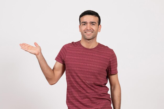 Jovem do sexo masculino com uma camiseta vermelho-escura em pé sobre um fundo branco de frente