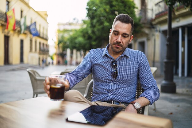 Jovem do sexo masculino com uma roupa formal sentado em um café ao ar livre bebendo uma bebida gelada