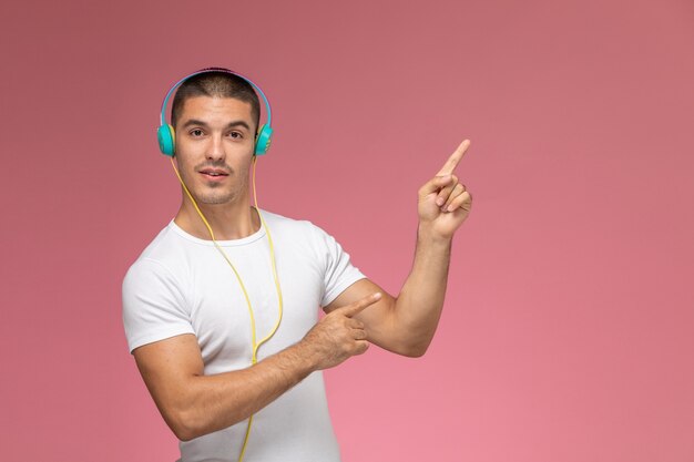 Jovem do sexo masculino de camiseta branca ouvindo música com os fones de ouvido na mesa rosa claro de frente