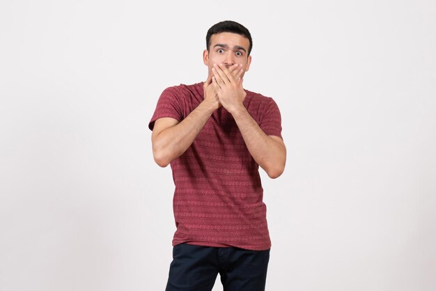 Jovem do sexo masculino de frente para a camiseta, posando com uma expressão de choque no fundo branco