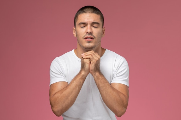 Foto grátis jovem do sexo masculino de frente para uma camiseta branca em oração, posando em fundo rosa