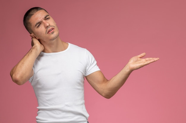 Jovem do sexo masculino em uma camiseta branca com dor de cabeça no pescoço em fundo rosa