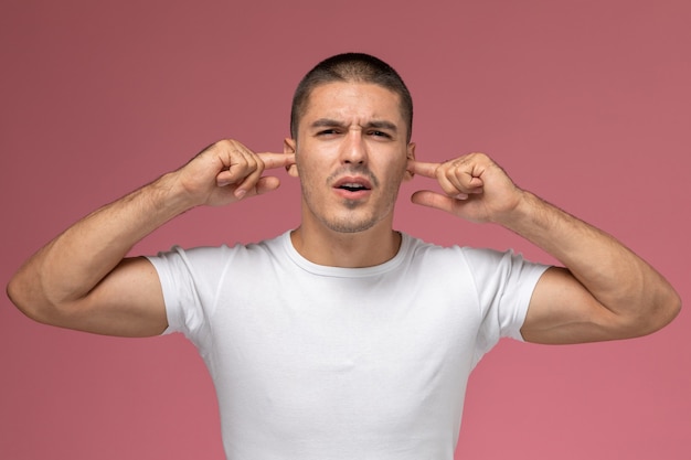 Jovem do sexo masculino em uma camiseta branca de frente colando as orelhas em um fundo rosa