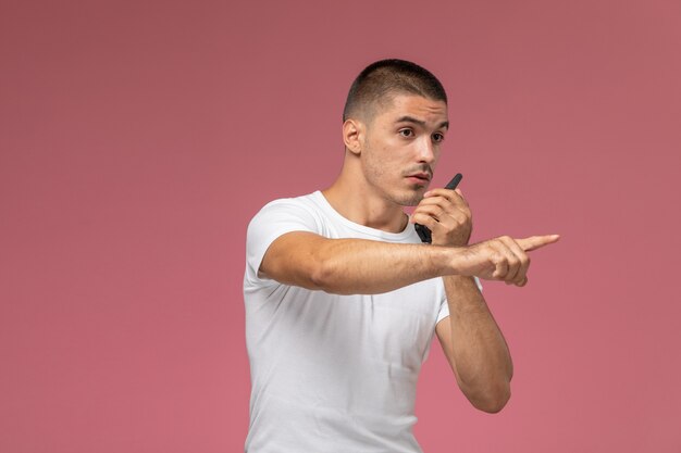 Jovem do sexo masculino em uma camiseta branca usando walkie-talkie no fundo rosa