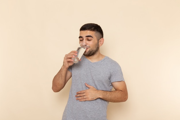 Jovem do sexo masculino em uma camiseta cinza bebendo água em bege