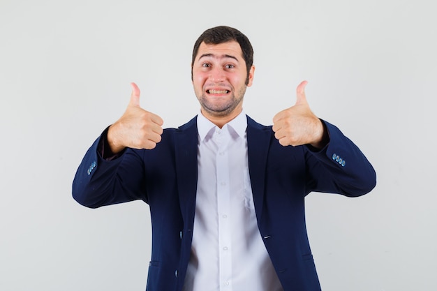 Jovem do sexo masculino mostrando dois polegares para cima com camisa e jaqueta e parecendo feliz