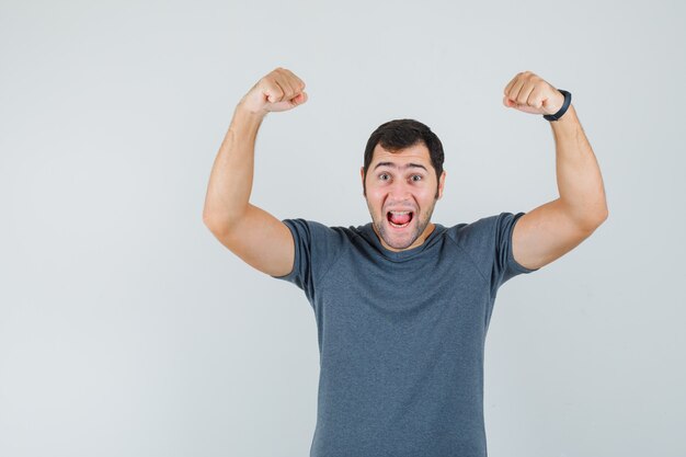 Jovem do sexo masculino mostrando gesto de vencedor em camiseta cinza e parecendo feliz