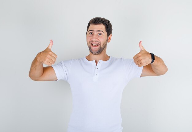 Jovem do sexo masculino mostrando os polegares para cima em uma camiseta branca e parecendo feliz