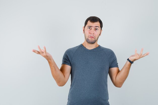 Jovem do sexo masculino mostrando um gesto desamparado em uma camiseta cinza e parecendo confuso