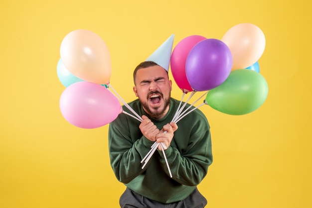 Jovem do sexo masculino segurando balões coloridos em um fundo amarelo de frente