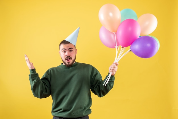 Jovem do sexo masculino segurando balões coloridos em um fundo amarelo de frente