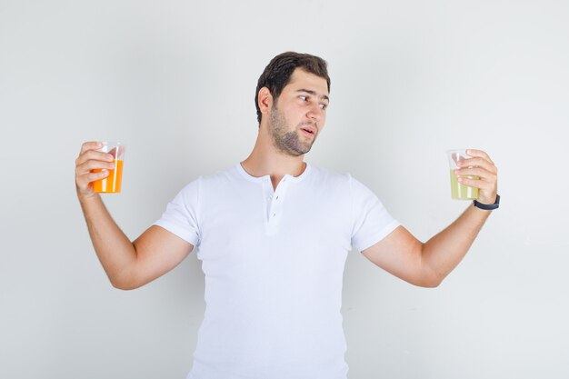 Jovem do sexo masculino segurando copos de bebida em uma camiseta branca e parecendo com sede