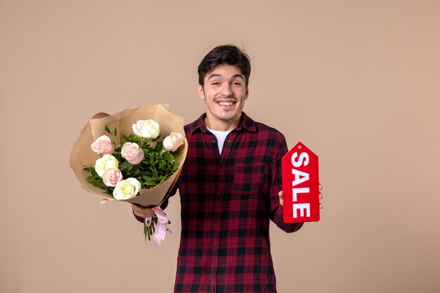 Jovem do sexo masculino segurando lindas flores e uma placa de identificação de venda na parede marrom.