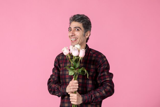 Jovem do sexo masculino segurando lindas rosas cor de rosa na parede rosa