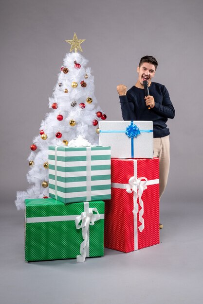 Jovem do sexo masculino segurando o microfone de frente com presentes na mesa cinza, presente de Natal, ano novo