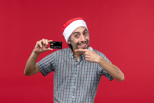 Jovem do sexo masculino segurando um cartão preto sobre o fundo vermelho