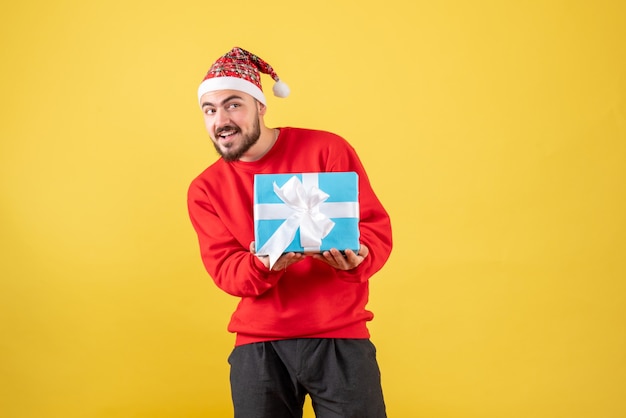 Jovem do sexo masculino segurando um presente de natal no fundo amarelo de frente