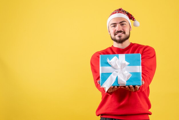 Jovem do sexo masculino segurando um presente de natal no fundo amarelo de frente