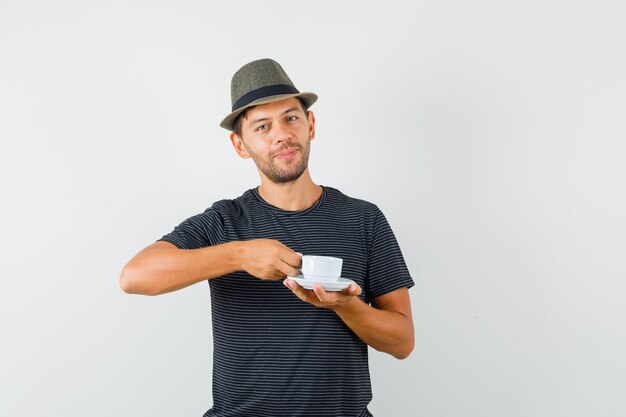 Foto grátis jovem do sexo masculino segurando uma xícara de café com um chapéu de camiseta e parecendo alegre