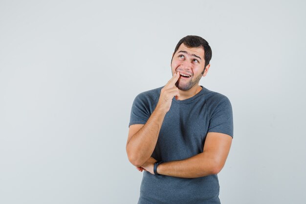 Jovem do sexo masculino sofrendo de dor de dente, vestindo uma camiseta cinza e parecendo desconfortável