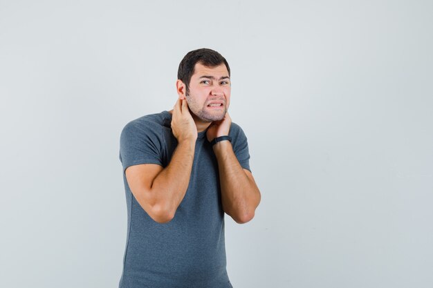 Jovem do sexo masculino sofrendo de dor no pescoço usando uma camiseta cinza e parecendo indisposto