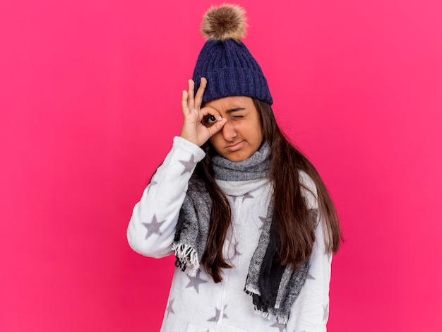 Jovem doente com chapéu de inverno e lenço mostrando gesto de olhar isolado em rosa