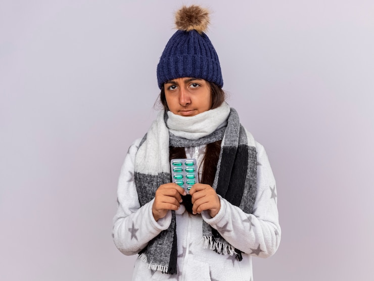 Foto grátis jovem doente com chapéu de inverno e lenço segurando comprimidos isolados no branco