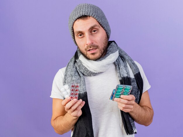 Jovem doente com chapéu de inverno e lenço segurando comprimidos isolados no fundo roxo
