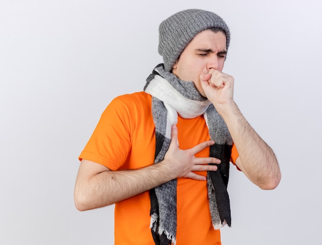 Foto grátis jovem doente com tosse com chapéu de inverno e lenço colocando a mão na boca isolado no branco