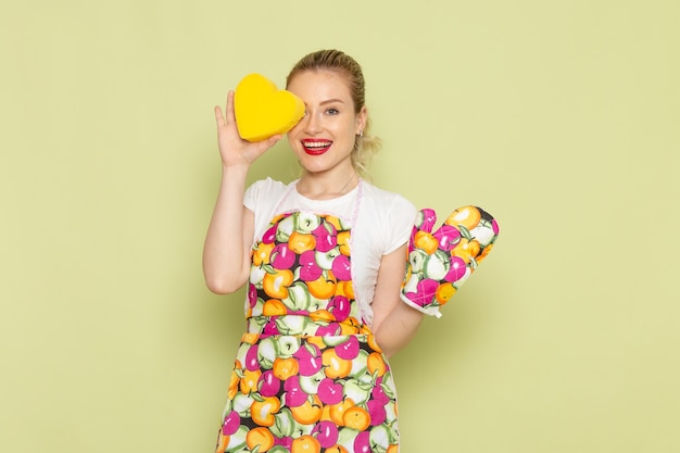 Jovem dona de casa com camisa e capa colorida segurando um coração amarelo no verde