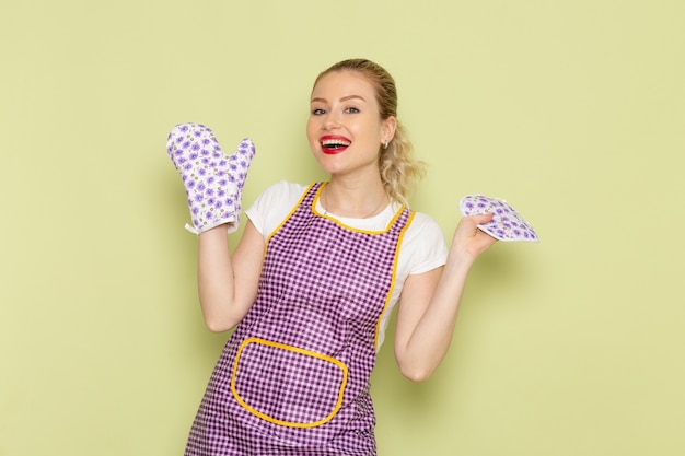 jovem dona de casa com camisa e capa roxa usando luvas de cozinha em verde