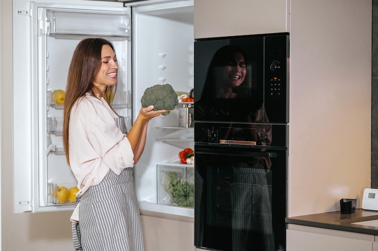 Foto grátis jovem dona de casa em pé perto da geladeira na cozinha