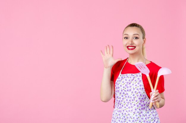 Jovem dona de casa posando com talheres na parede rosa