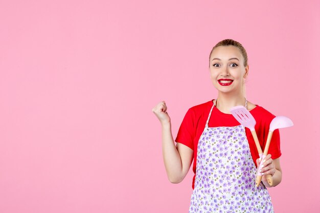 Foto grátis jovem dona de casa posando com talheres sorrindo na parede rosa