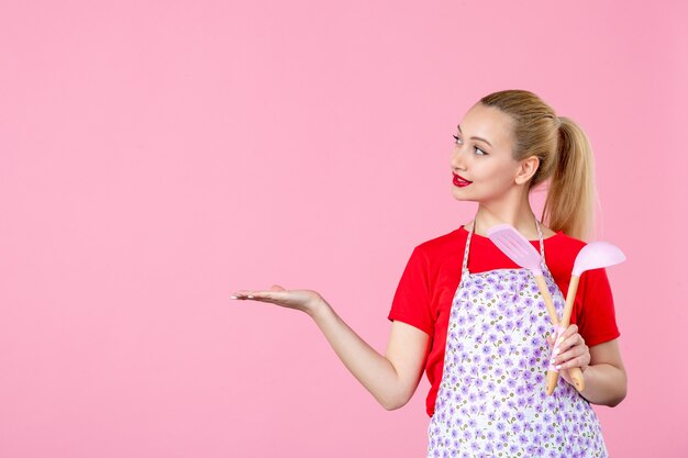 Jovem dona de casa segurando talheres na parede rosa de frente