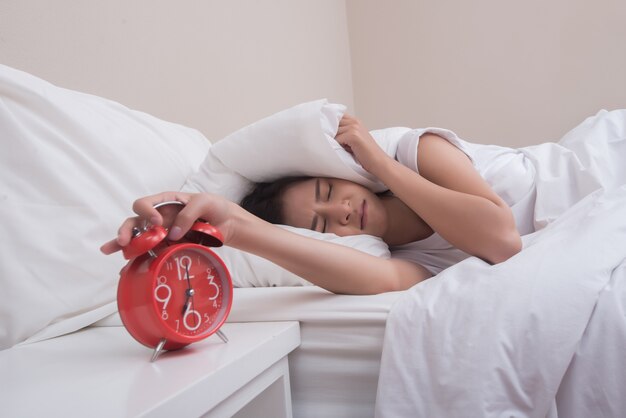 Jovem, dormindo na cama e despertador no quarto da manhã