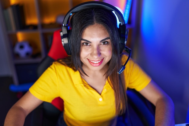 Foto grátis jovem e bela mulher árabe streamer sorrindo confiante sentado na mesa na sala de jogos