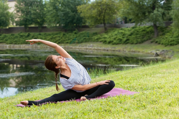 Jovem e bela mulher fazendo exercícios de ioga no parque verde. Estilo de vida saudável e conceito de aptidão.