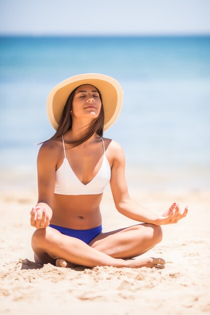 Jovem e bela mulher meditando na praia perto do mar