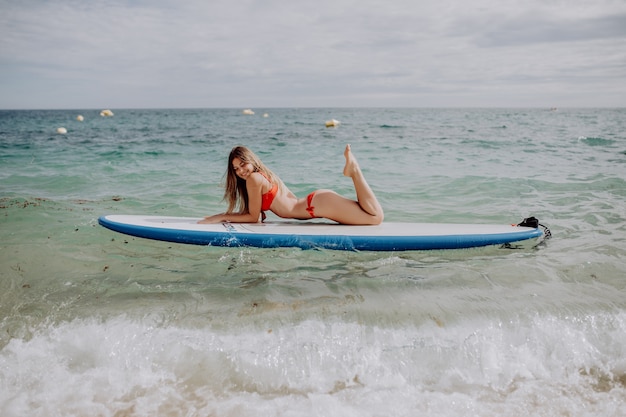 Jovem e bela mulher relaxante no mar em uma prancha de SUP.
