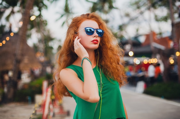 Jovem e bela mulher sexy, estilo hippie, cabelo ruivo, viajante, top verde, mala laranja, férias de verão, viajar, óculos de sol, ouvir música, fones de ouvido, óculos de sol, viagem tropical