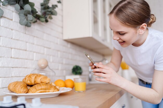 Jovem e bela mulher tirando foto no celular de croissants