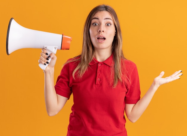 Foto grátis jovem e bonita caucasiana surpresa segurando um alto-falante e a mão aberta na laranja