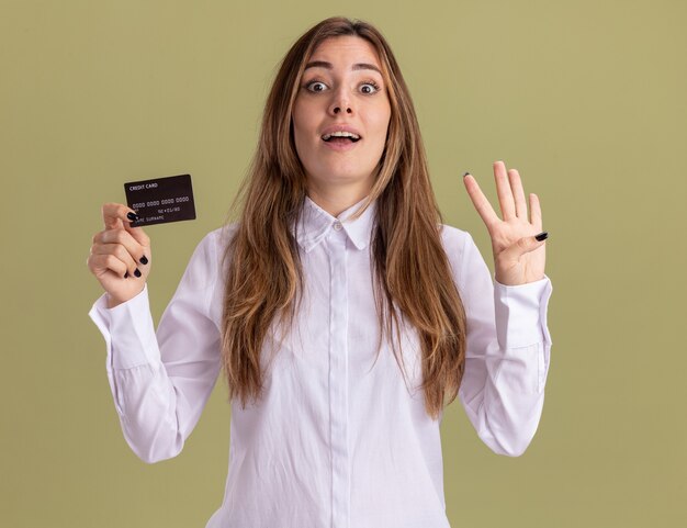 Jovem e bonita caucasiana surpresa segurando um cartão de crédito e gesticulando quatro com os dedos