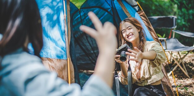 Jovem e bonita fotografia amiga por câmera digital enquanto está sentada na barraca de acampamento na floresta Jovens mulheres do grupo asiático viajam acampando ao ar livre