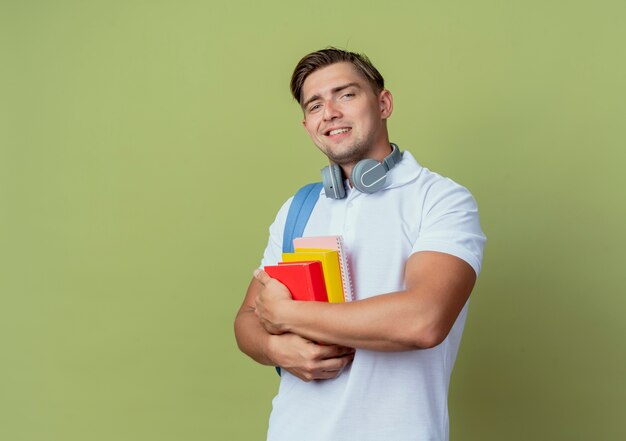 Jovem e bonito estudante sorridente usando uma bolsa com livros sobre verde oliva