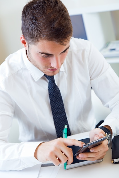 Foto grátis jovem e bonito trabalhando em seu escritório com telefone celular.